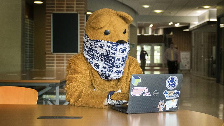 The Nittany Lion using a laptop while wearing a mask.